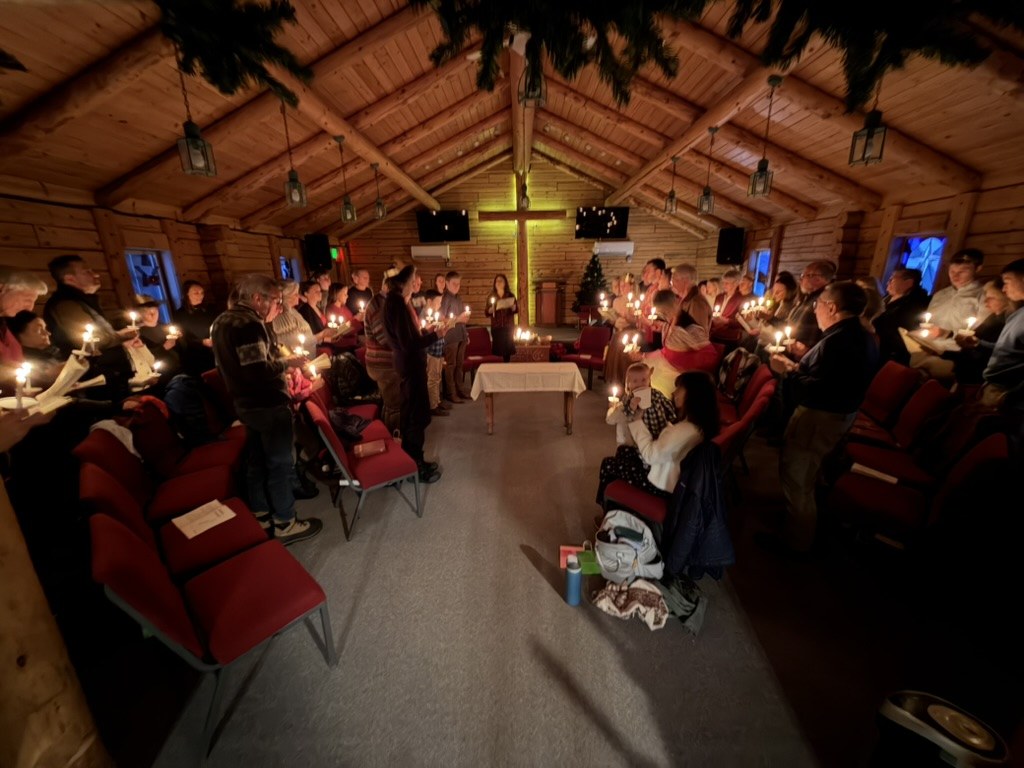 Candlelight Christmas Eve service in the log cabin church, the congregation holding candles before the cross