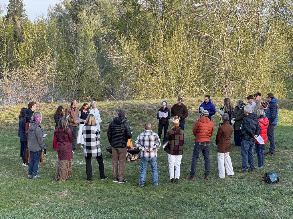 The fellowship standing in a circle around the Easter fire in a spring meadow