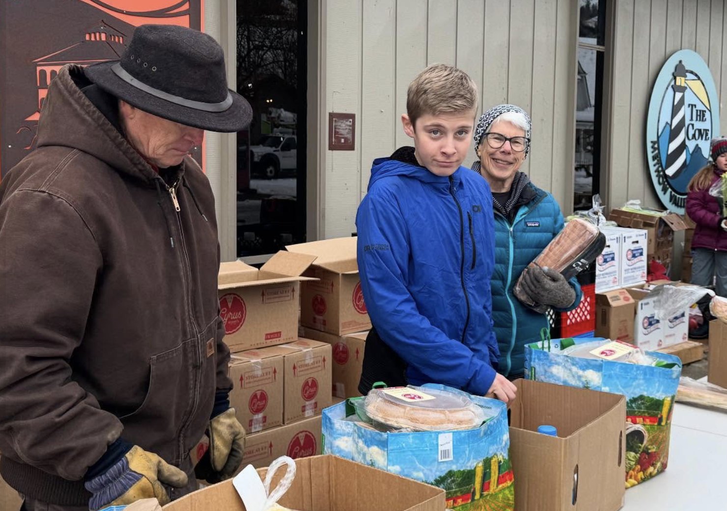 Volunteers of all ages packing grocery bags outside The Cove food bank in winter